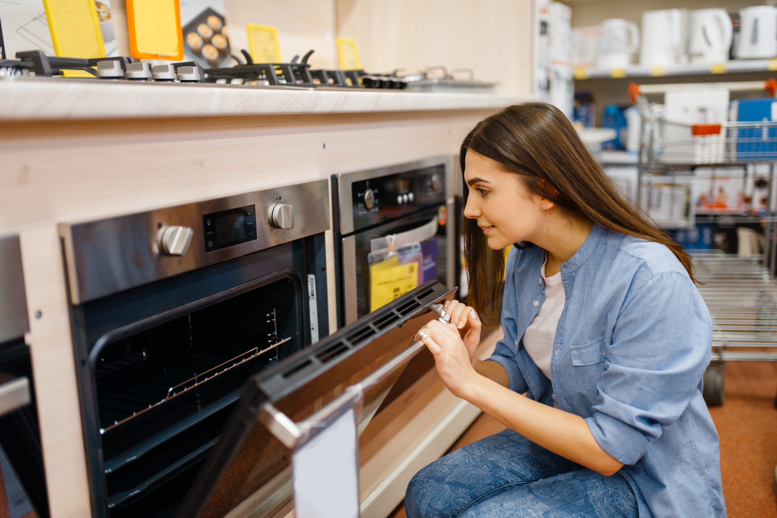 Young woman choosing electric oven in electronics store. Female person buying home electrical appliances in market, housewife looking goods in shop
